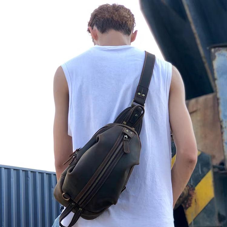 Uomo con zaino a tracolla in pelle marrone, indossa maglietta bianca senza maniche. Accessorio moda casual, esterno urbano.