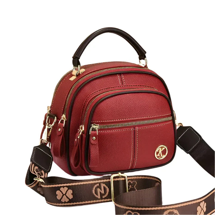 Borsa a tracolla in pelle rossa con manico superiore, cerniere dorate e logo decorativo. Design elegante, ideale per moda donna e accessori.