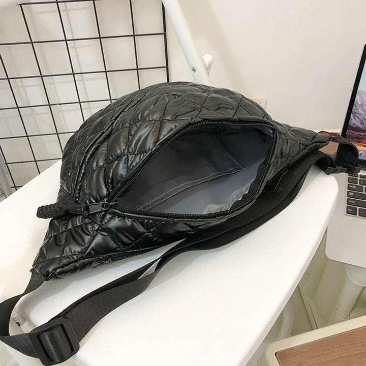 Borsa a tracolla nera trapuntata aperta su sedia bianca, design moderno, chiusura a zip, ideale per moda urbana e viaggi.