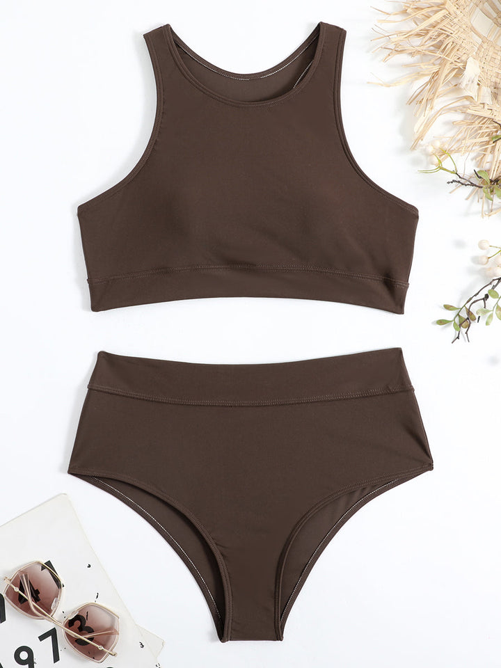 Costume da bagno donna marrone scuro a due pezzi, top sportivo e slip a vita alta, su sfondo bianco con occhiali da sole e decorazioni naturali.