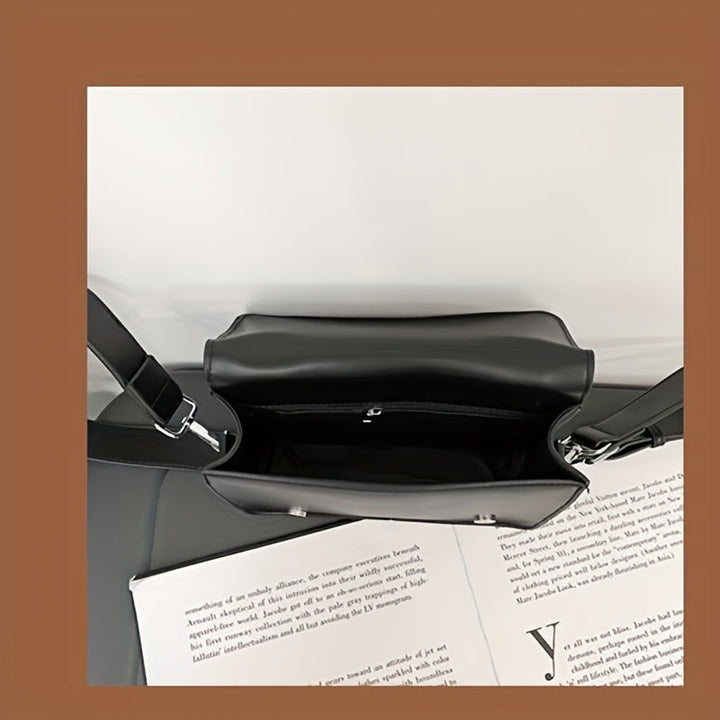 Borsa a tracolla nera in pelle, vista dall'alto, con interno spazioso e chiusura a zip, su sfondo di pagine di libro. Elegante e moderna.