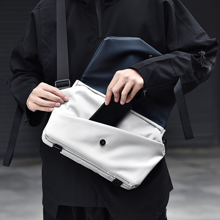 Borsa a tracolla moderna in tessuto bianco, con tasca frontale e chiusura a bottone, indossata da una persona in abbigliamento nero.