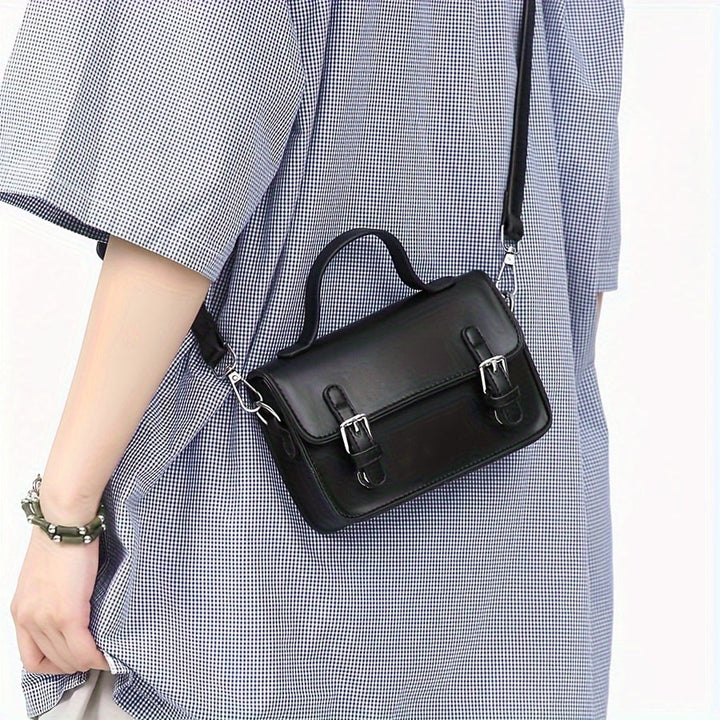 Borsa a tracolla nera in pelle, design elegante con fibbie argentate, indossata su abito a quadri. Accessorio moda donna, stile casual chic.