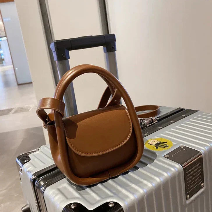 Borsa a tracolla marrone su valigia argentata in aeroporto. Accessori da viaggio eleganti, borsa in pelle, valigia rigida.