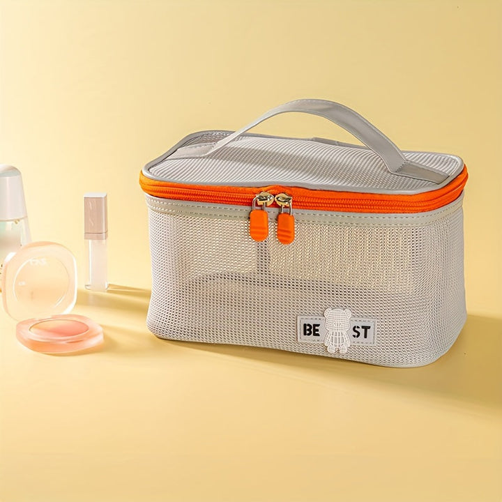 Borsa cosmetica in rete grigia con cerniera arancione, manico superiore, su sfondo giallo. Accessori trucco accanto. Organizzatore da viaggio elegante.