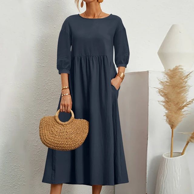 Donna con abito lungo blu scuro, maniche a tre quarti, tasche laterali, borsa in paglia. Moda elegante, abbigliamento casual femminile.