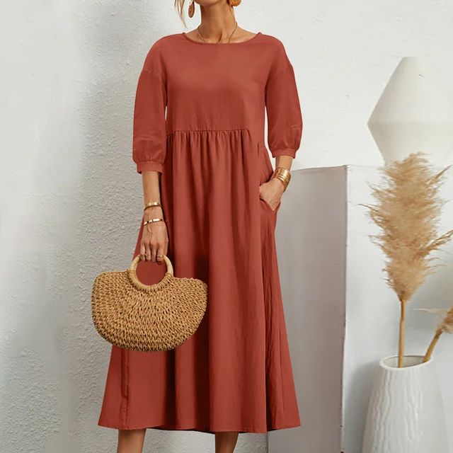 Abito lungo rosso terracotta con maniche a tre quarti, borsa in paglia intrecciata, sfondo bianco minimalista, moda donna elegante e casual.
