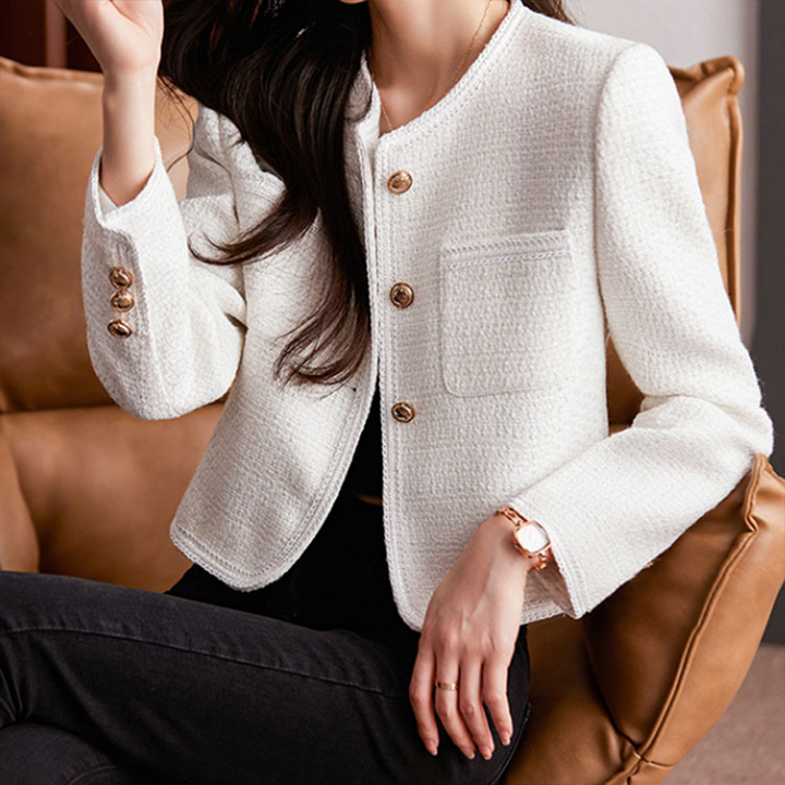 Giacca donna elegante bianca in tweed, con bottoni dorati, tasca frontale, indossata su divano marrone. Moda femminile, abbigliamento chic.