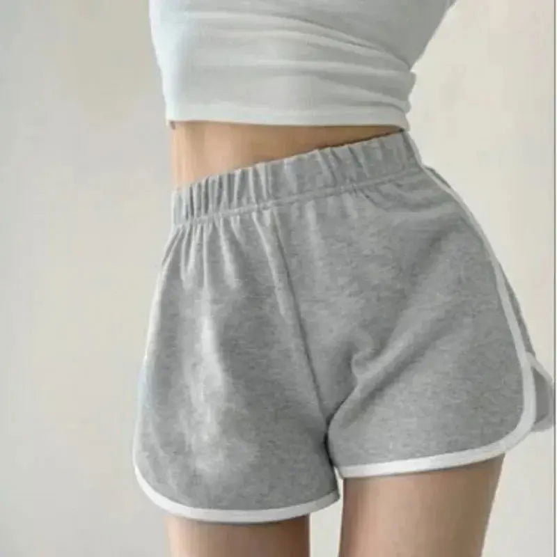 Donna in top bianco e pantaloncini grigi sportivi, vita alta, elastico, comodi per allenamento e tempo libero. Abbigliamento casual estivo.