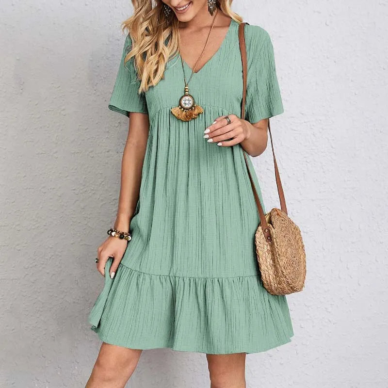 Abito estivo verde donna, maniche corte, scollo a V, tessuto leggero, borsa a tracolla in paglia, moda casual, look estivo elegante.