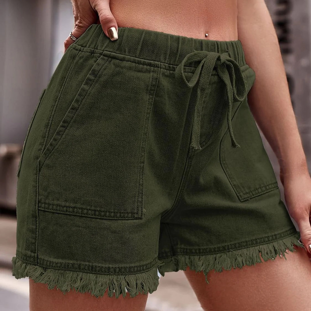 Shorts verdi in denim con frange, tasche frontali e laccio in vita. Moda estiva donna, abbigliamento casual, stile urbano.