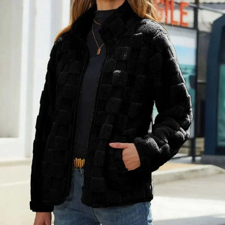 Giacca nera in pile a quadri, donna, con zip frontale, indossata su maglia grigia e jeans. Moda autunnale, abbigliamento casual elegante.