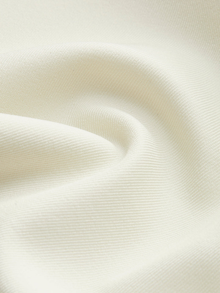 Tessuto bianco crema, texture morbida e ondulata, ideale per abbigliamento elegante e arredamento. Materiale di alta qualità, versatile e raffinato.