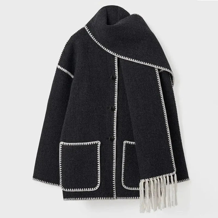 Cappotto nero in lana con bordi bianchi, tasche frontali e sciarpa abbinata con frange. Elegante e caldo, ideale per l'inverno.