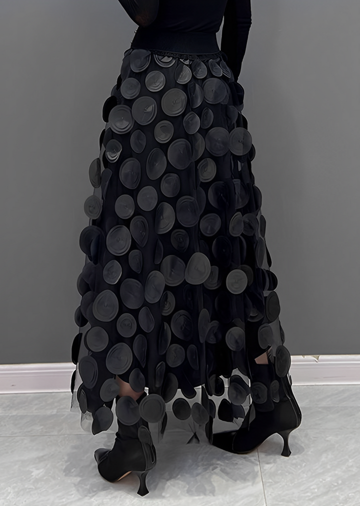 Gonna lunga nera con cerchi decorativi, design elegante e moderno, indossata con stivali neri su sfondo grigio. Moda femminile autunno inverno.
