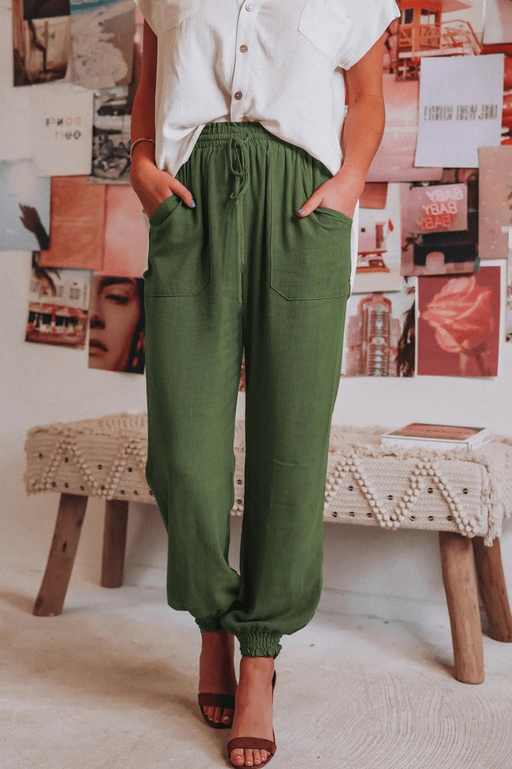 Donna in camicia bianca e pantaloni verdi, posa casual in interni boho chic. Moda femminile estiva, abbigliamento comodo ed elegante.