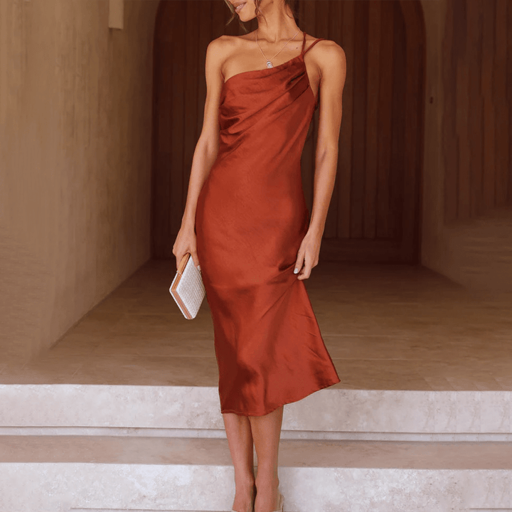 Abito midi elegante in raso rosso, monospalla, indossato da donna con pochette bianca. Perfetto per eventi serali e cerimonie.