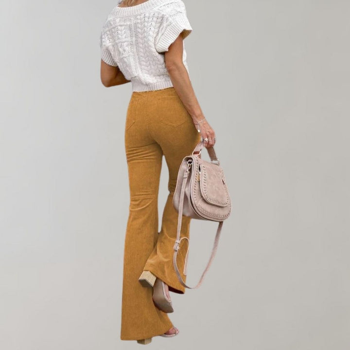 Donna con pantaloni a zampa color senape, maglia bianca lavorata a maglia, borsa a tracolla beige. Moda autunnale elegante e casual.