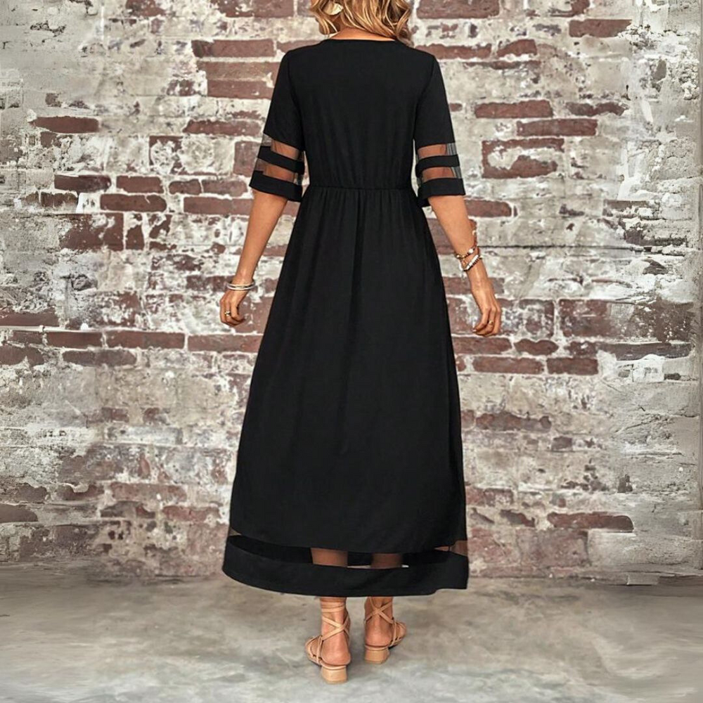 Donna in abito lungo nero elegante con dettagli trasparenti, sfondo muro di mattoni. Moda femminile, abbigliamento estivo, stile casual chic.