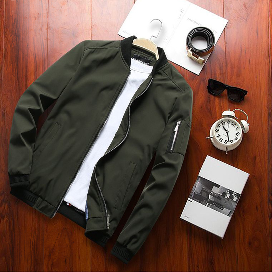 Giacca bomber verde oliva su sfondo in legno, con t-shirt bianca, occhiali da sole, orologio e cintura. Moda uomo casual, abbigliamento autunnale.