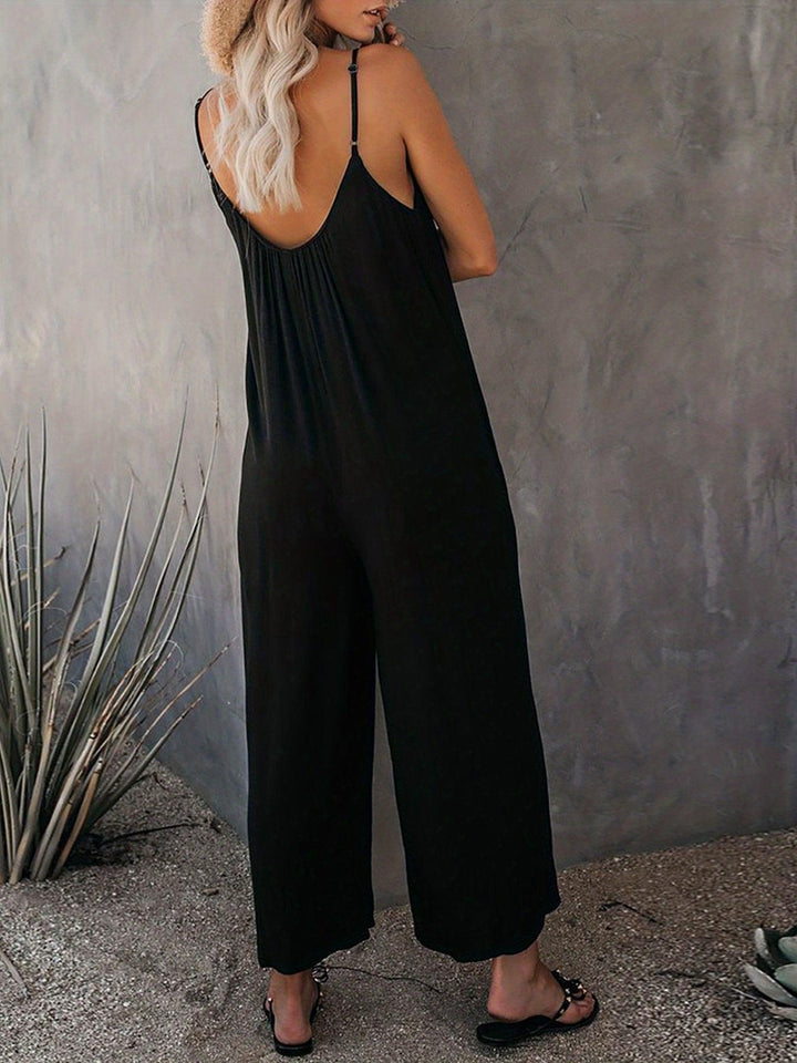 Donna in tuta nera estiva, spalline sottili, schiena scoperta, sandali neri, sfondo grigio. Moda casual elegante, abbigliamento donna estivo.