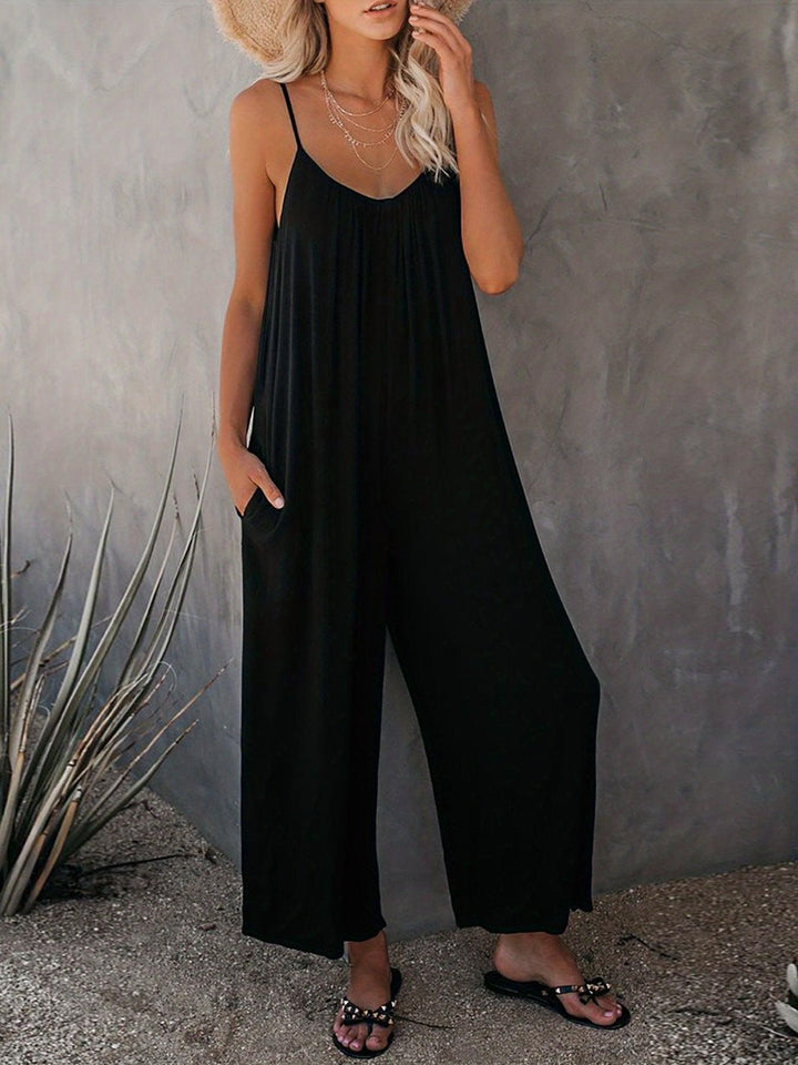 Donna con tuta nera estiva, sandali e cappello di paglia. Moda casual elegante, abbigliamento estivo donna, tuta lunga con spalline sottili.