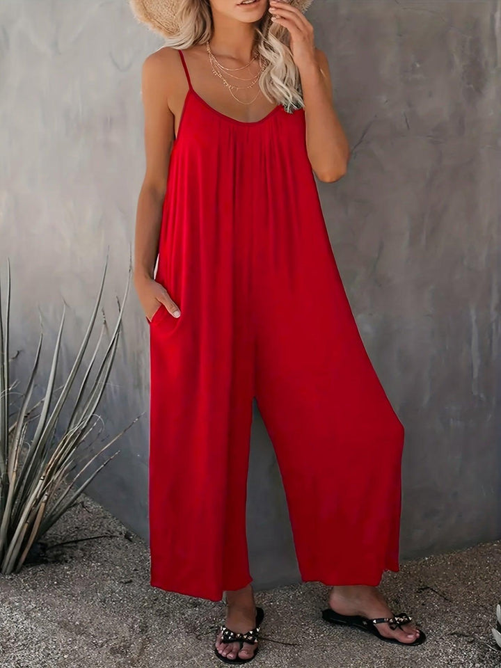 Donna con tuta rossa estiva, spalline sottili, sandali neri, sfondo grigio. Moda femminile, abbigliamento casual elegante, tendenza estiva.