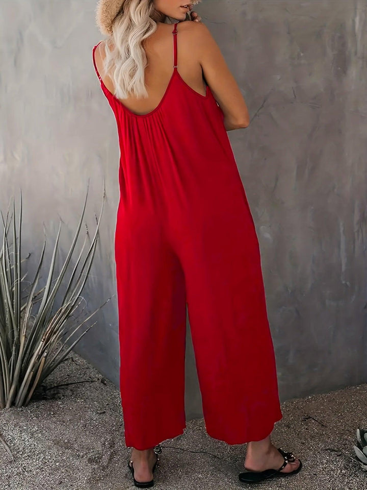 Donna in tuta rossa estiva, spalline sottili, sfondo grigio, piante decorative. Moda femminile, abbigliamento casual elegante.