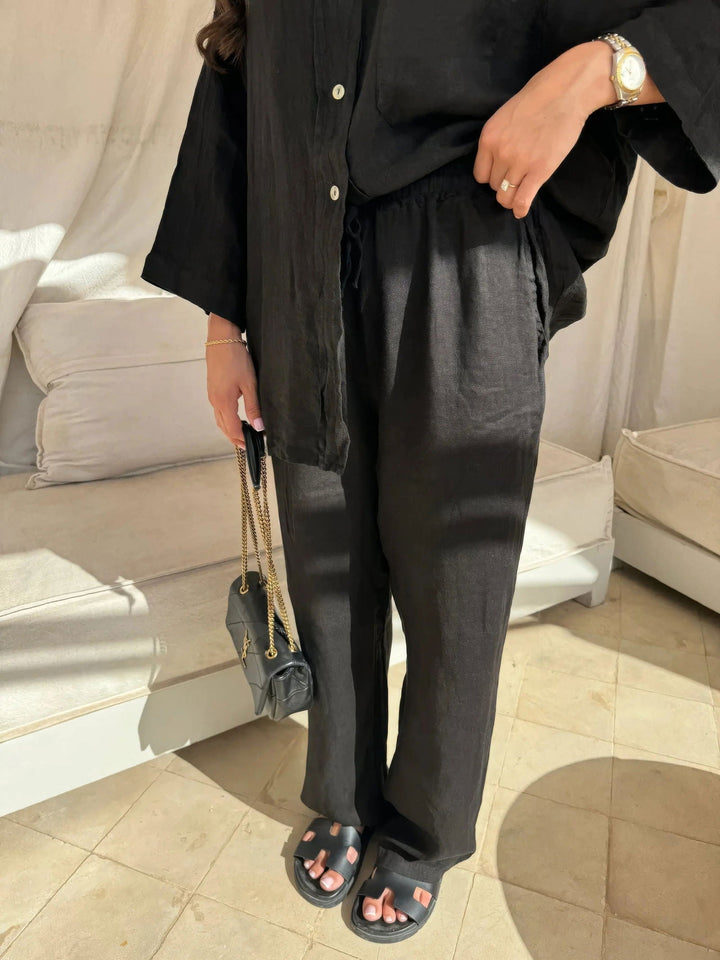 Donna in abbigliamento nero casual, con camicia e pantaloni larghi, sandali neri e borsa a tracolla. Stile minimalista ed elegante.