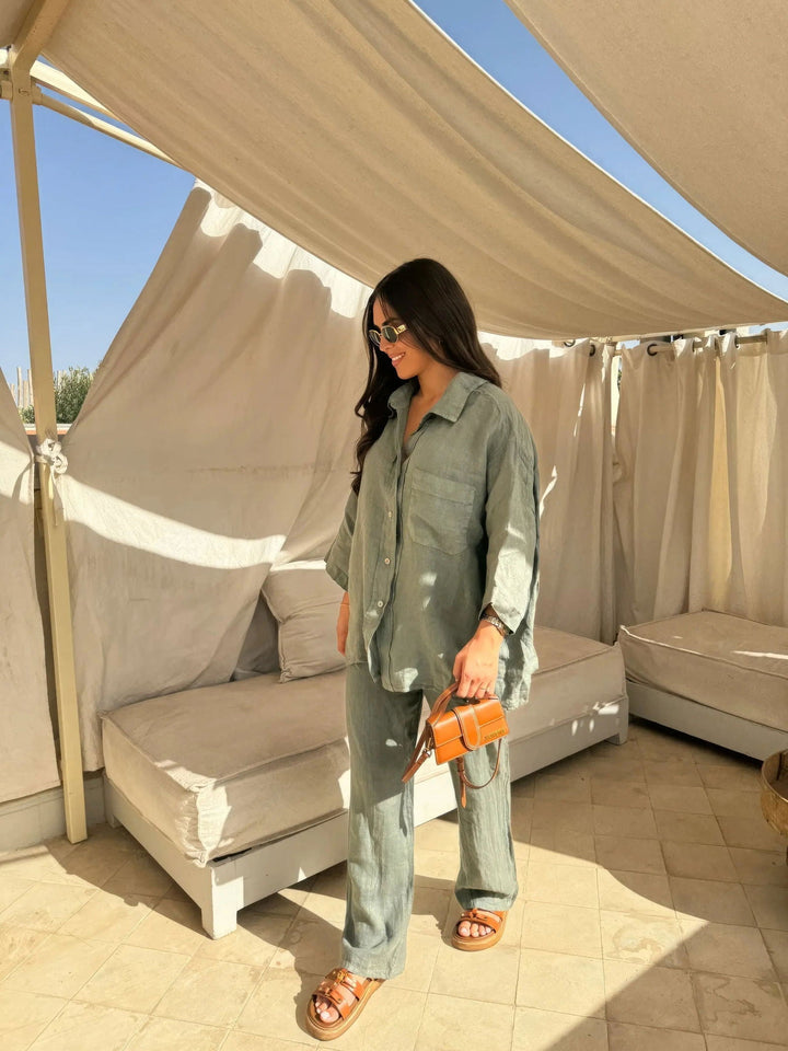 Donna con abito coordinato verde, occhiali da sole e borsa arancione in un'area lounge all'aperto. Moda estiva, stile casual chic.