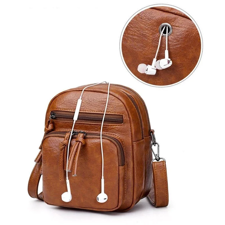 Zaino in pelle marrone con foro per auricolari, tasche multiple e tracolla regolabile. Design elegante e pratico per uso quotidiano.