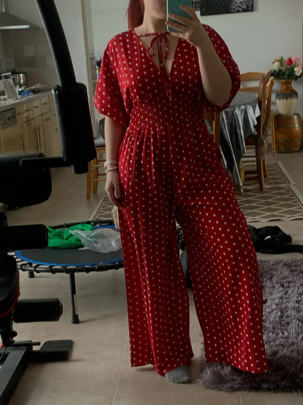 Donna in tuta rossa a pois bianchi, scollo a V, maniche corte, in una cucina moderna. Abbigliamento estivo elegante, moda femminile casual.