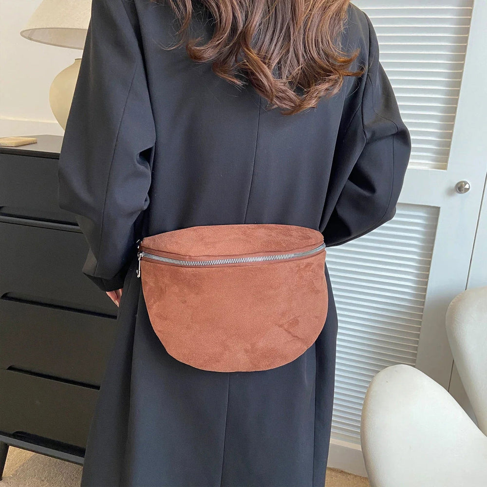 Donna con marsupio in pelle scamosciata marrone, indossa cappotto nero. Accessorio moda casual, pratico per viaggi e passeggiate urbane.