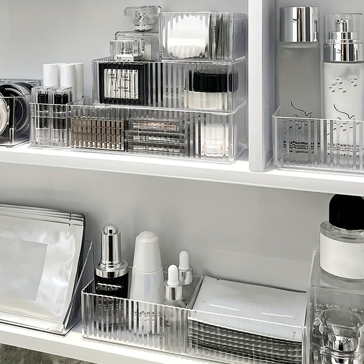 Organizzatore trasparente per cosmetici su scaffale bianco, contenente profumi, creme, sieri e trucchi. Soluzione elegante per l'archiviazione del trucco.