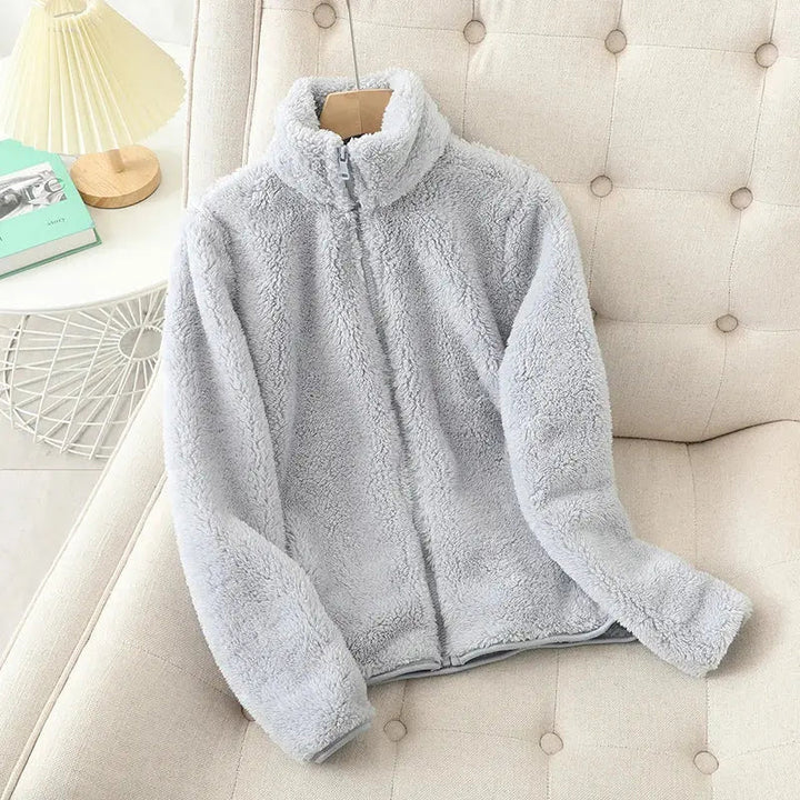 Giacca in pile grigio chiaro su divano beige, design con zip, morbida e calda, ideale per l'inverno. Abbigliamento casual, moda donna.