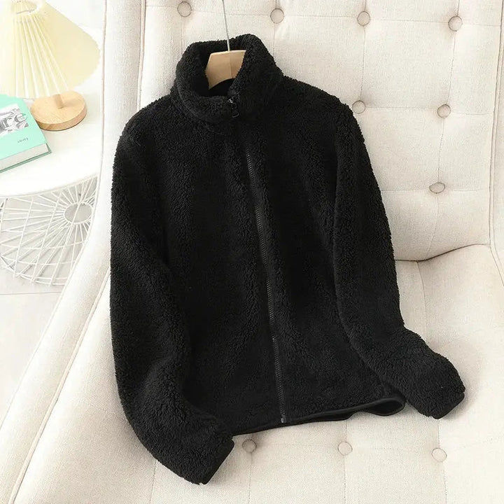 Giacca in pile nero su sedia beige, design morbido e caldo, ideale per l'inverno. Moda casual, abbigliamento donna, stile confortevole.