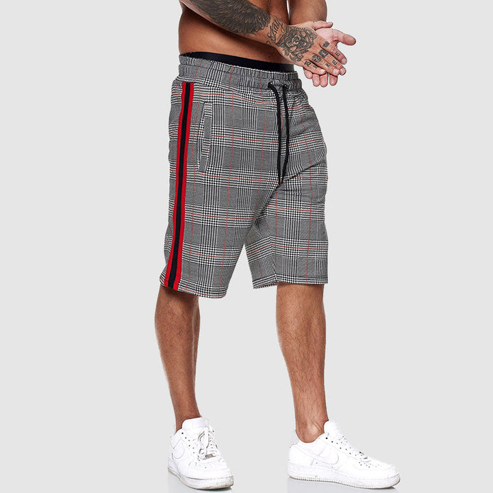Pantaloncini uomo a quadri grigi con righe rosse, elastico in vita, tasche laterali, stile casual sportivo, indossati con scarpe bianche.