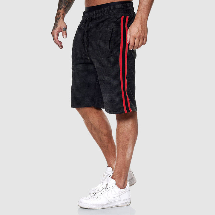Pantaloncini uomo neri con righe rosse laterali, stile casual sportivo, indossati con scarpe da ginnastica bianche. Ideali per moda estiva.