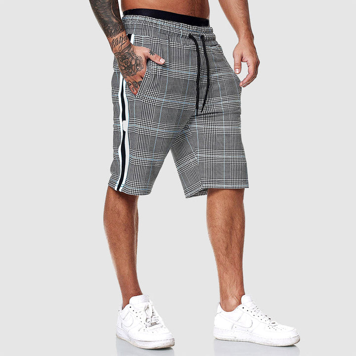 Pantaloncini uomo a quadri grigi con strisce laterali bianche, elastico in vita, tasche, abbinati a scarpe sportive bianche.