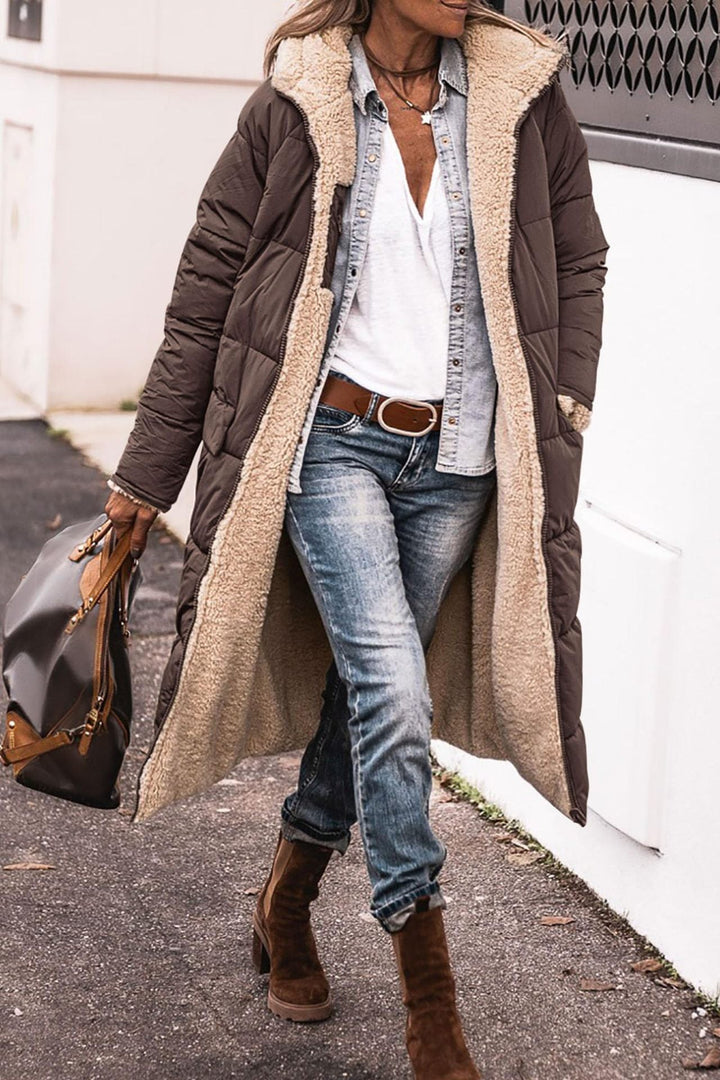 Donna con cappotto lungo marrone imbottito, jeans, stivali marroni e borsa in pelle. Moda invernale casual, abbigliamento caldo e confortevole.