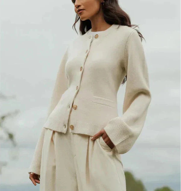 Donna con cardigan beige in lana, abbottonato, maniche lunghe, abbinato a pantaloni coordinati. Moda autunnale elegante e minimalista.