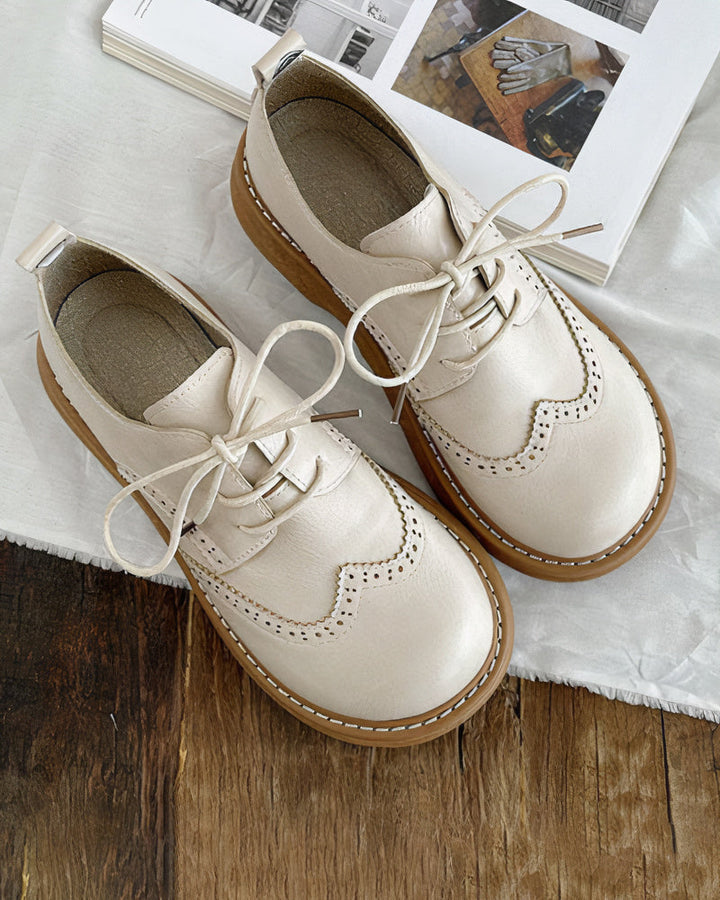 Scarpe stringate in pelle bianca da donna su sfondo di legno e tessuto, design elegante con suola marrone, perfette per look casual e formali.