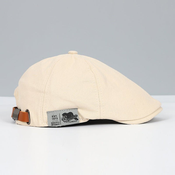 Cappello piatto beige in cotone con cinturino regolabile in pelle marrone, etichetta "Quality Fashion". Elegante accessorio moda uomo.