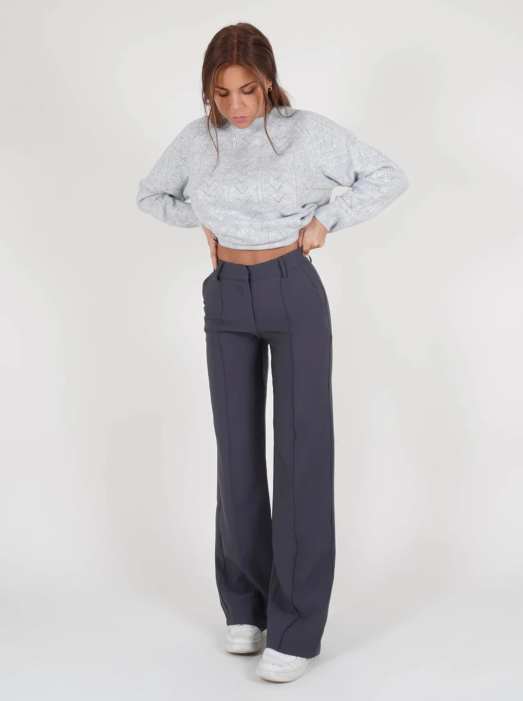 Donna con maglione grigio lavorato a maglia e pantaloni blu scuro a vita alta, scarpe bianche. Moda casual autunnale, abbigliamento femminile elegante.