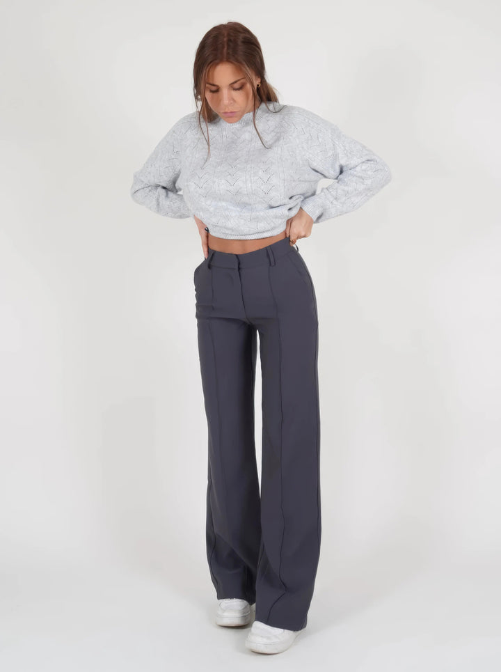Donna con maglione grigio lavorato a maglia e pantaloni blu scuro a vita alta, scarpe bianche. Moda casual autunnale, abbigliamento femminile elegante.