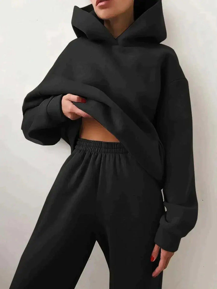 Donna con felpa nera oversize e pantaloni coordinati, moda casual, abbigliamento comodo, stile streetwear, tendenza autunno inverno.