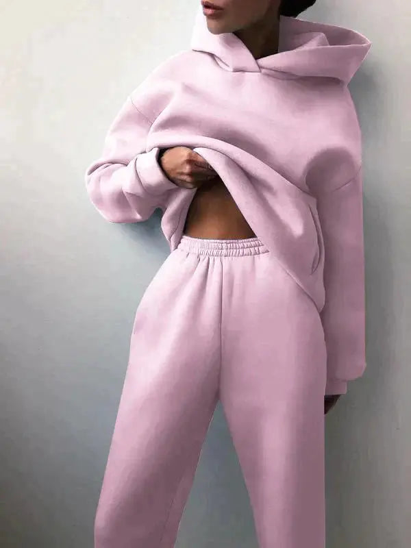 Donna in tuta sportiva rosa pastello, felpa con cappuccio e pantaloni comodi. Abbigliamento casual, moda donna, stile rilassato.