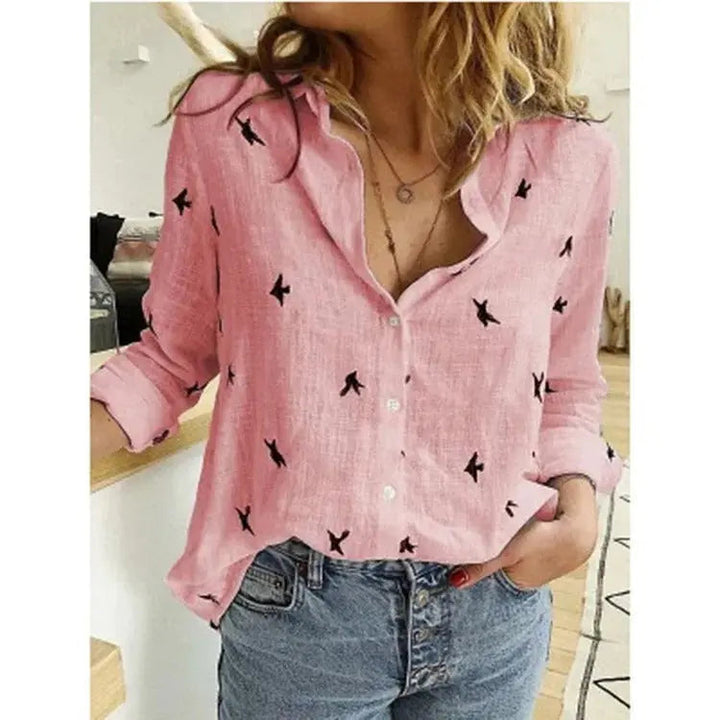 Camicia rosa donna con stampa uccelli neri, maniche lunghe arrotolate, abbinata a jeans a vita alta. Moda casual, stile primaverile.