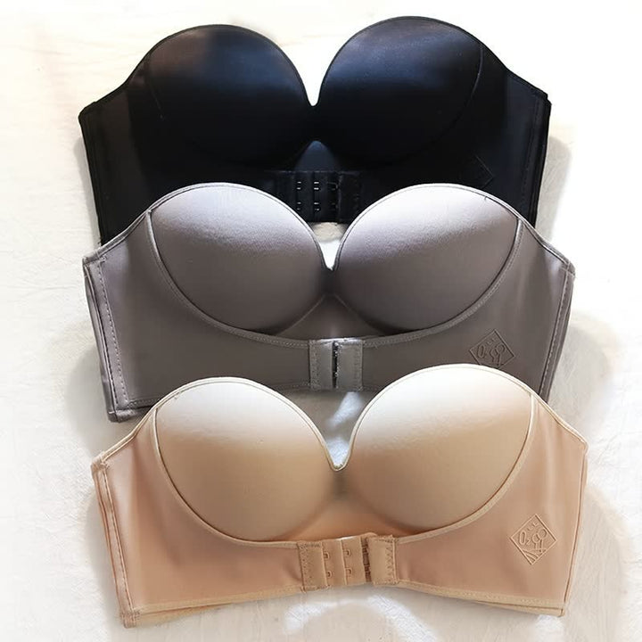 Tre reggiseni senza spalline in nero, grigio e beige su sfondo bianco. Design liscio, coppe imbottite, chiusura frontale. Intimo femminile elegante.
