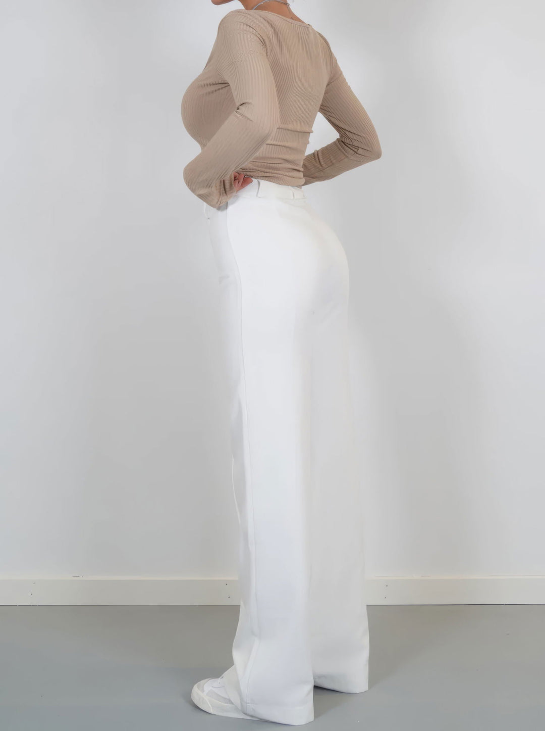 Donna in pantaloni bianchi a vita alta, abbinati a maglia beige a maniche lunghe. Stile elegante, moda femminile, abbigliamento casual chic.